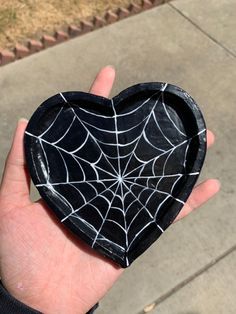 a hand holding a black and white heart shaped box with spider webs on it