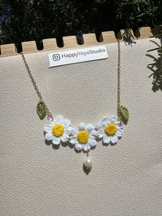 a white and yellow necklace with flowers hanging from it's sides on a display shelf