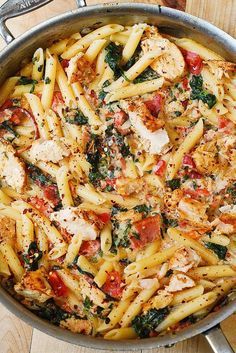 a pan filled with pasta covered in chicken and spinach next to a wooden table