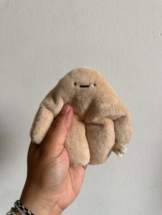 a hand holding a small stuffed animal in front of a white wall with writing on it