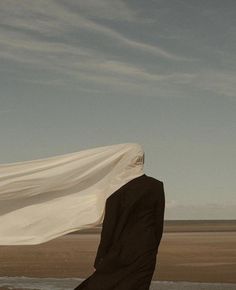 a woman in black and white is standing on the beach with her veil flying over her head