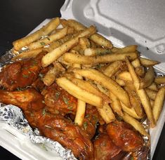 chicken wings and french fries in a takeout container with tinfoil wrapper on the side