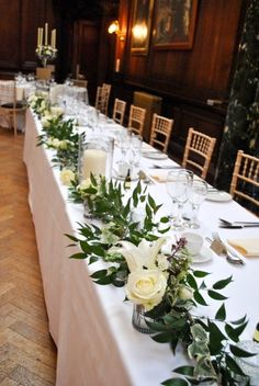 the long table is set with white flowers and greenery for an elegant wedding reception