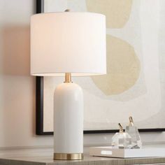 a white lamp sitting on top of a table next to a framed art piece and a painting