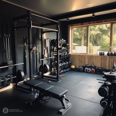 a home gym with black walls and lots of equipment on the floor in front of large windows