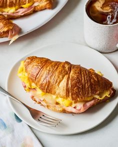 a croissant sandwich on a white plate next to a cup of coffee and a fork