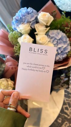 a person holding up a card that says bliss on it with flowers in the background