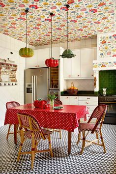 a red table and chairs in a room with colorful wallpaper on the ceiling above it