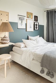 a white bed sitting next to a window with curtains on the windowsill and pictures above it