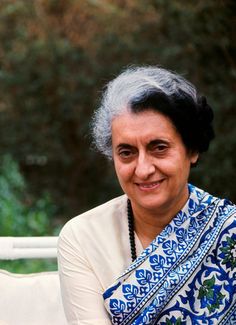 an older woman is smiling while sitting on a white bench with trees in the background