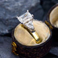 an engagement ring with a diamond in it sitting on top of a wooden box next to some rocks