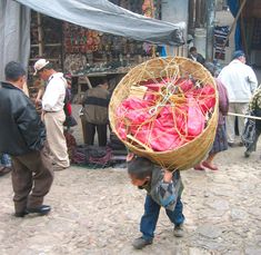 a young boy carrying a basket full of red cloths on top of his head