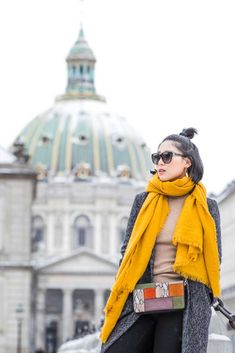 a woman wearing sunglasses and a yellow scarf stands in front of a building with a dome