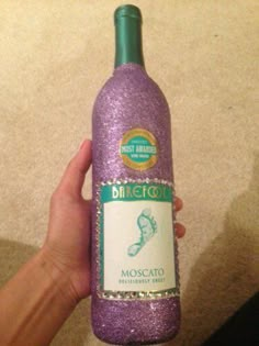 a hand holding a purple wine bottle with glitter on it