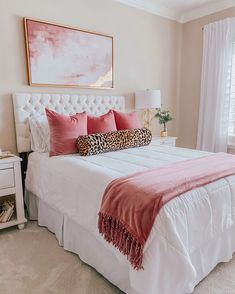 a white bed topped with pink pillows and a leopard print throw pillow on top of it