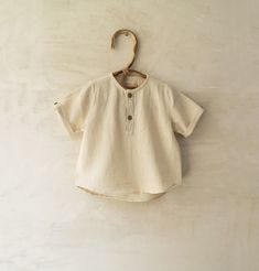 m o d e l  MITRA a short sleeve boys top in natural white organic cotton, round piped neck, placket with contrasting inner fabric, coconut shell buttons, rounded at base and longer at back, handembroidery on yoke and placket f a b r i c kala cotton: indian indigenous handspun rainfed organic cotton  s i z e s 6 m  I  68  chest      22'' length    12'' 1 yr  I  80  chest      24'' length    13 ½'' 2 yr  I  92 chest      26'' length    15'' 3 - 4 yr  I 104  chest      28'' length    17'' 5 - 6 yr Neutral Cotton Summer Shirt, Short Sleeve Cotton T-shirt In Neutral Color, Neutral Cotton Short Sleeve T-shirt, Neutral Short Sleeve Cotton T-shirt, Off White Cotton Tops For Everyday, Everyday Cream Organic Cotton Tops, Short Sleeve Organic Cotton Tops For Summer, Organic Cotton Short Sleeve Tops For Summer, Summer Organic Cotton Short Sleeve Tops