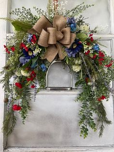 a wreath with red, white and blue flowers is hanging on the front door frame