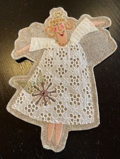 an embroidered angel ornament on a wooden table with white lace and beading