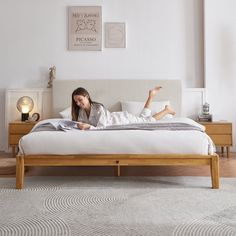 a woman laying on top of a bed in a room with white walls and wooden furniture