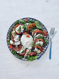 a blue and white plate filled with salad on top of a table next to a fork