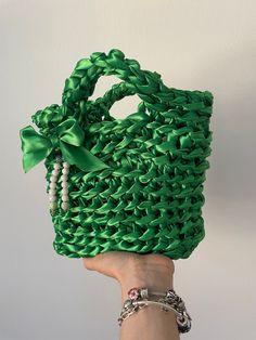 a hand is holding a green purse made out of plastic beads and chains with a bow on it