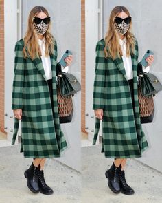 a woman in a green coat and black boots is holding a handbag while wearing a face mask