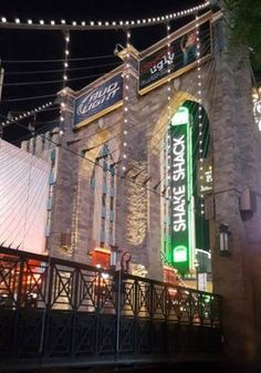 the outside of a building lit up at night with lights strung from it's sides