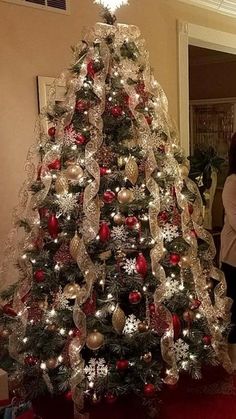 a christmas tree is decorated with red and silver ornaments, while a woman stands next to it