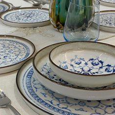 a table set with blue and white plates, silverware and flowers in vases