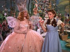 two women in dresses standing next to each other with christmas decorations on the wall behind them