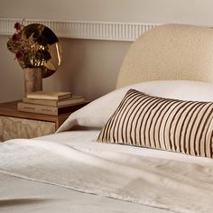 a bed with white sheets and pillows on top of it next to a vase filled with flowers