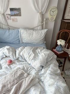 an unmade bed with white sheets and blue comforter in a small room next to a chair