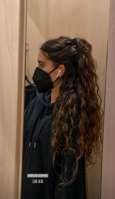 a woman wearing a black face mask standing in front of a door with long hair