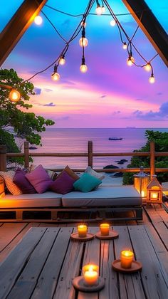 an outdoor seating area with lit candles on the floor and ocean in the background at dusk