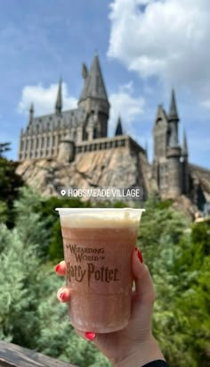 a person holding up a drink in front of hog potter's castle at universal studios