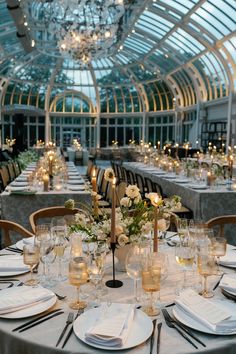 a table set up for a formal dinner in a glass walled dining room with chandelier