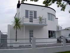 a white house with a palm tree in front of it and cars parked on the street