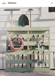 an old pallet with gardening tools on it and a hose attached to the wall