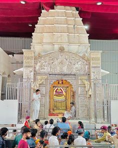 a group of people sitting in front of a white structure with a man standing on top of it