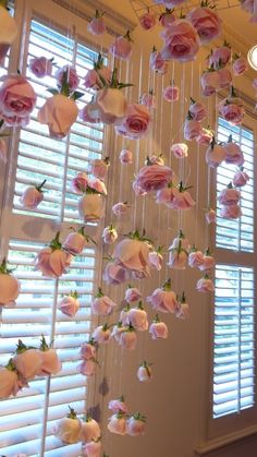 pink and white flowers hanging from the ceiling in front of windows with blinds on them