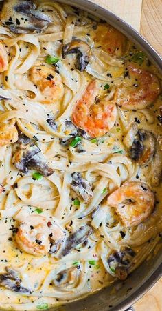 a pan filled with shrimp and pasta on top of a wooden table