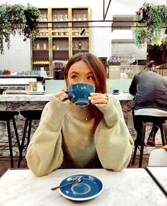 a woman sitting at a table drinking from a cup