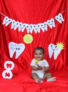 a baby sitting in front of a red backdrop with white teeth and decorations on it