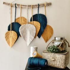 three different colored leaves hanging on a wall next to a basket with yarn and twine