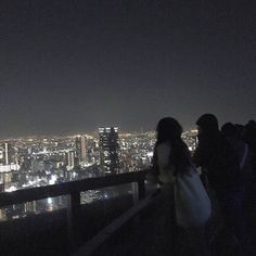 people standing on top of a tall building looking at the city lights in the distance