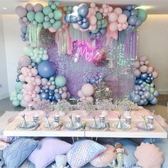 a table topped with lots of balloons next to a wall covered in confetti