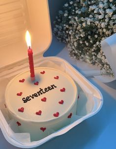 a white cake with red hearts on it in a box next to flowers and a candle