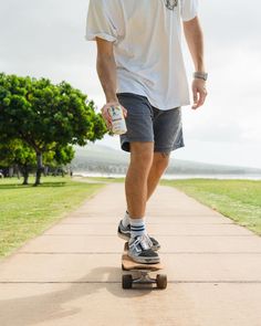 a man riding a skateboard down a sidewalk next to a tree and grass covered field