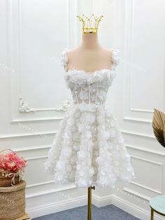 a white dress with flowers and a gold crown on the top is sitting on a mannequin