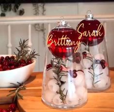 two glass vases filled with snowballs and christmas decorations on top of a wooden table